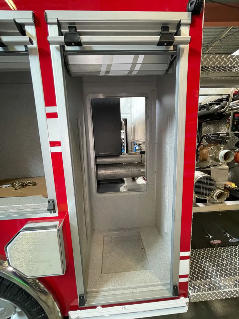 Exterior view of small fire truck showing cab, body compartments, and wheel/tire area.